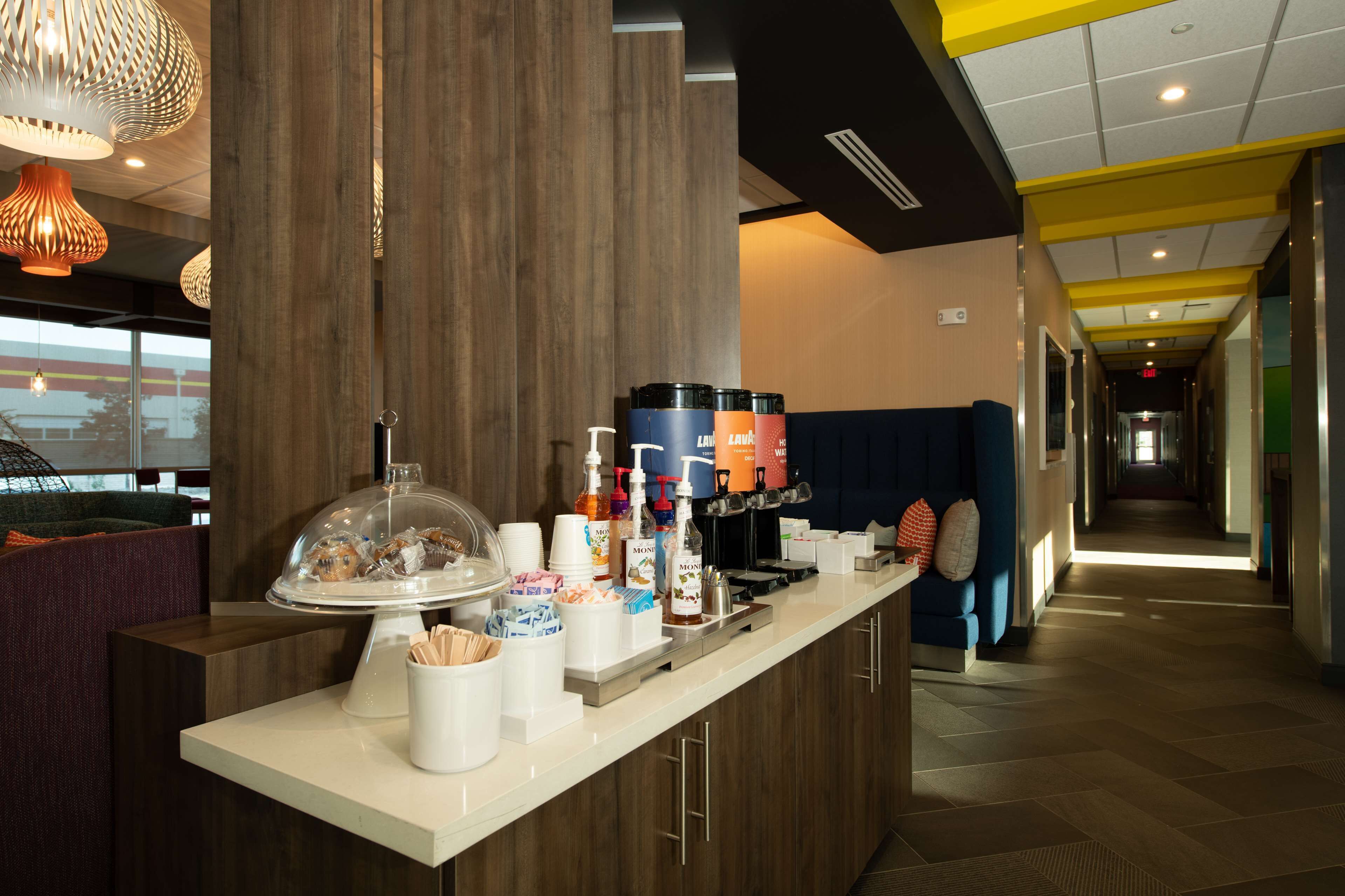 A hotel reception area with a counter displaying food and drink items, a seating area with a blue couch, and a corridor leading to other parts of the hotel.