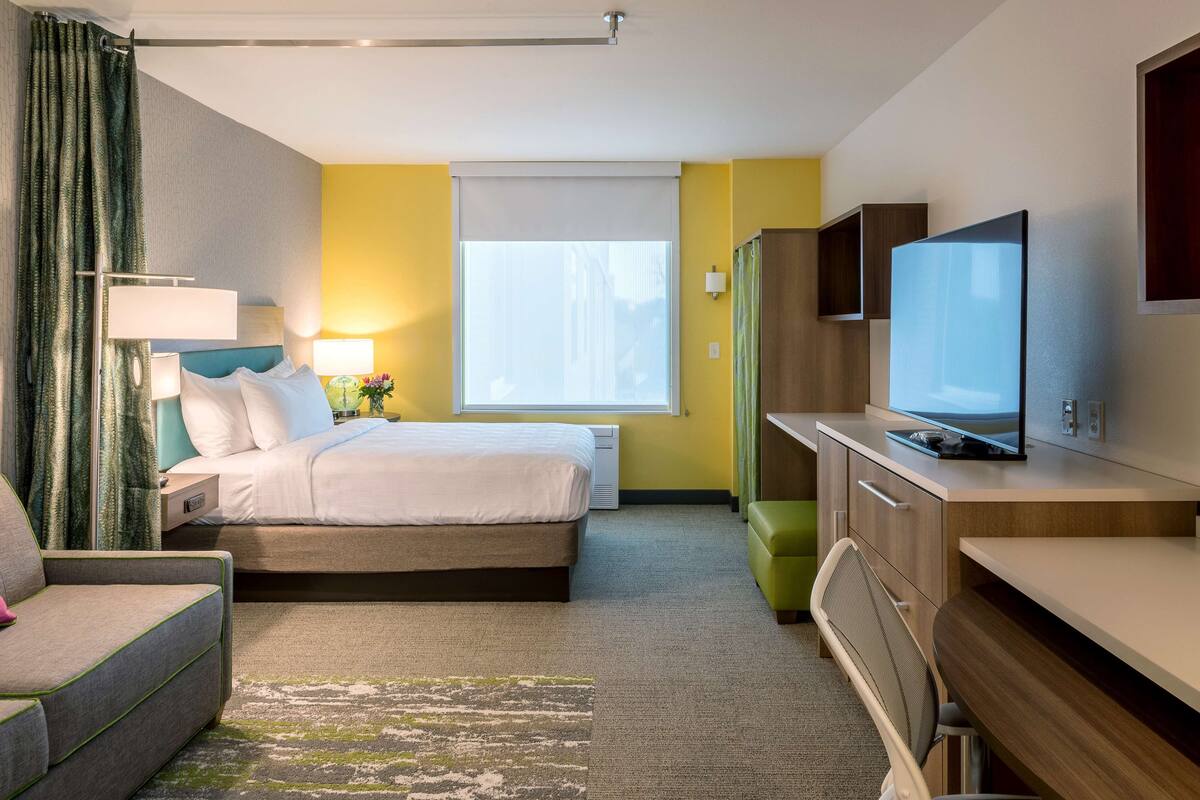 Une chambre d’hôtel avec un lit, un bureau, une télévision, une chaise et une fenêtre.