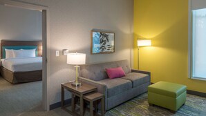 Una habitación de hotel con cama, sofá, una mesita, lámpara y un reposapiés verde.