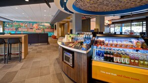 A modern restaurant interior with a mural of Manchester, a self-service beverage station, and a counter with stools. - Tru by Hilton Manchester Downtown (Manchester)