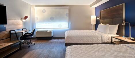 A hotel room with two beds, a desk, a chair, a TV, and a window with blinds.