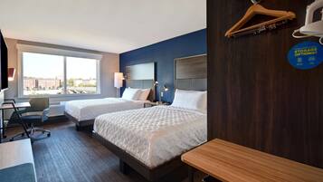 Habitació d'hotel amb dos llits, escriptori, cadira i una finestra gran que ofereix vista a la ciutat.
