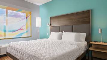 A modern hotel room with a large bed, a nightstand, a wall-mounted lamp, and a large abstract painting.
