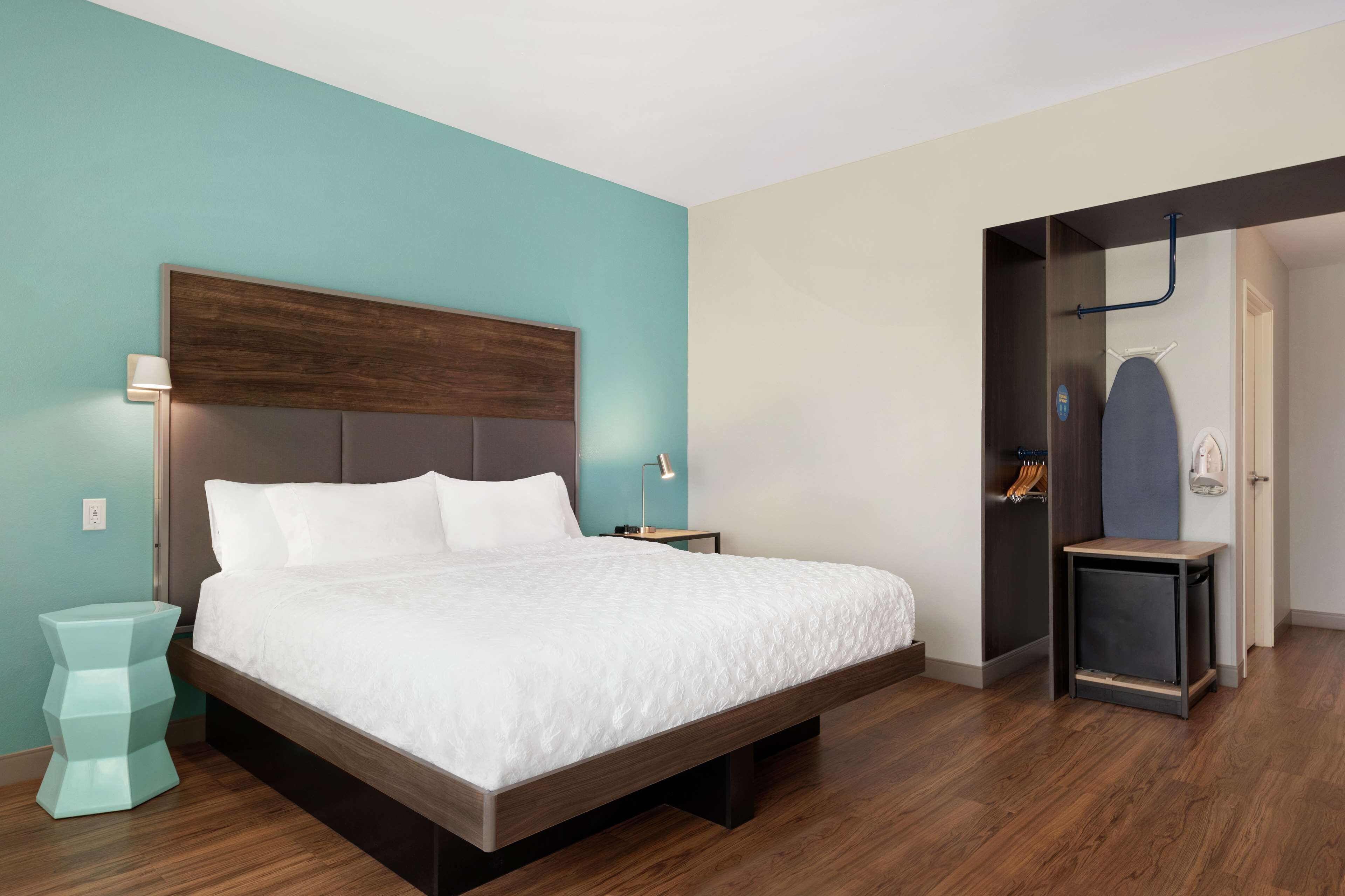 A modern bedroom with a large bed, wooden headboard, and a teal accent wall.