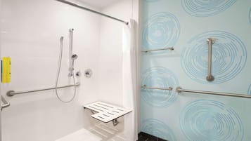 A modern bathroom with a shower, grab bars, and a white tiled floor.
