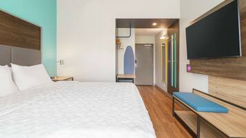 Una habitación de hotel moderna con una cama grande, un banco, un televisor de pantalla plana y zona de ducha.