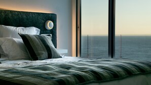 A modern bedroom with a large bed, a headboard with a circular light, and a view of the ocean through large windows. - Casa Emnitan - Begur (Begur)