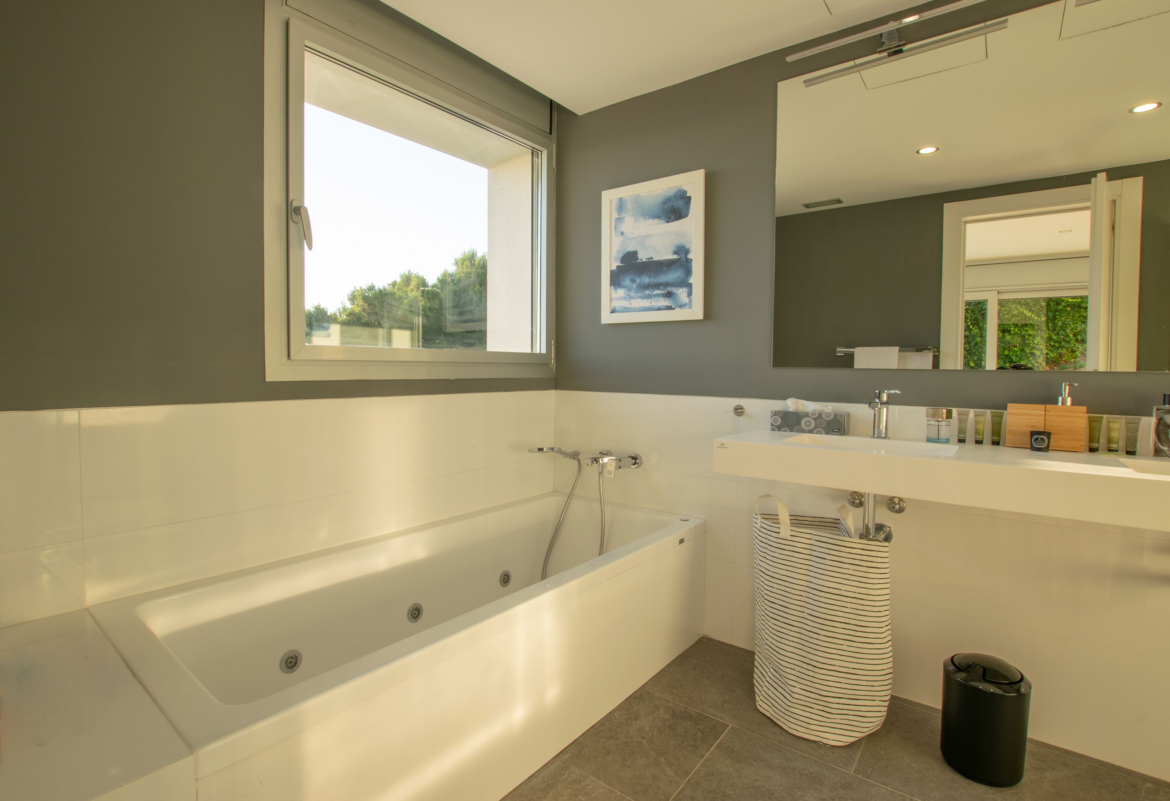 A modern bathroom with a bathtub, a large mirror, and a window.
