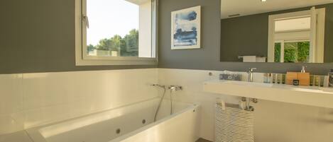 A modern bathroom with a bathtub, a large mirror, and a window.