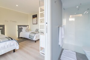 Een hotelkamer met twee bedden, een douchecabine van glas en een zichtbare handdoekrek.