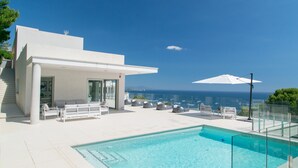 A modern pool area with a clear view of the sea, white outdoor furniture, and a glass-enclosed pool. - Casa Emnitan - Begur (Begur)