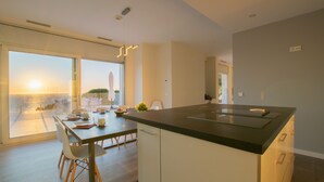 A modern kitchen with a large island, dining area with chairs, and a view of the sea through large windows. - Casa Emnitan - Begur (Begur)