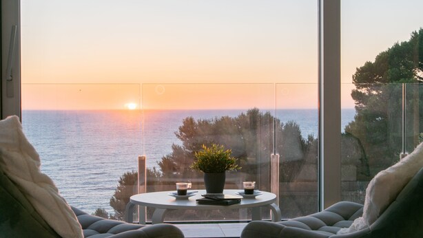 A room with a view of the sunset over the sea, a round table with a potted plant, and two chairs. - Casa Emnitan - Begur (Begur)