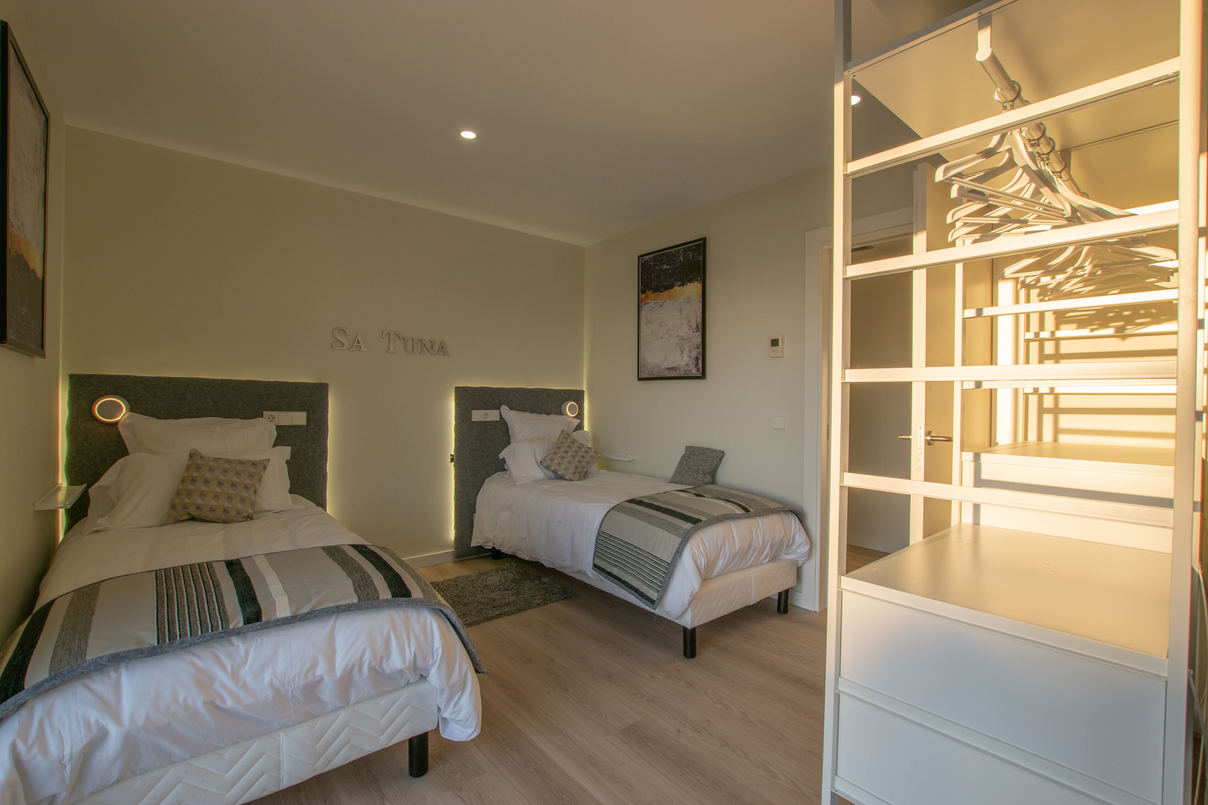 A bedroom with two beds, a wardrobe, and a headboard with a built-in shelf.