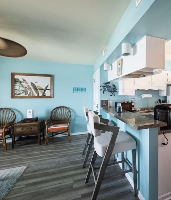 A modern kitchen with a bar area, wooden chairs, and a dining table. - Oceanfront Carolina Beach condo, panoramic views and pool! Top floor sunrises! (Carolina Beach)
