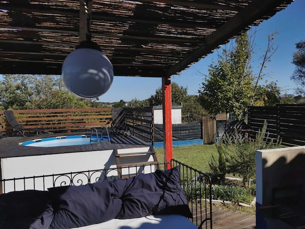 A pool area with a pergola overhead, a hot tub, and a fenced garden.