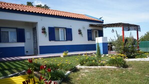 A two-story house with a blue and white exterior, a tiled roof, and a garden with yellow and red flowers. - Herdade Palma T1  (country house) (Moita)