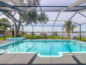 A swimming pool with a view of a lake and a covered area with chairs and a basketball hoop. - Fantastic Water Front Home on the Chain of Lakes (Winter Haven)