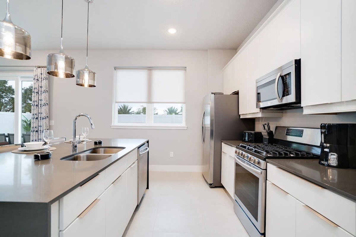 A modern kitchen with stainless steel appliances, a large island with a sink, and pendant lighting.