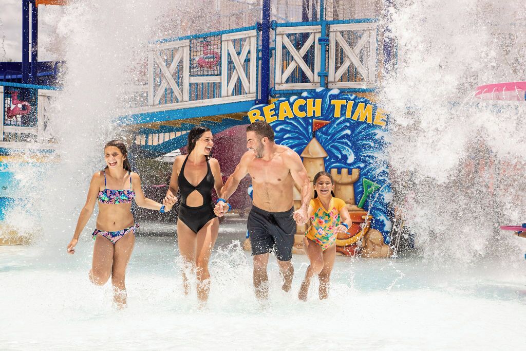 Parque acuático con un cartel que dice 'Beach Time', salpicaduras de agua y gente disfrutando.