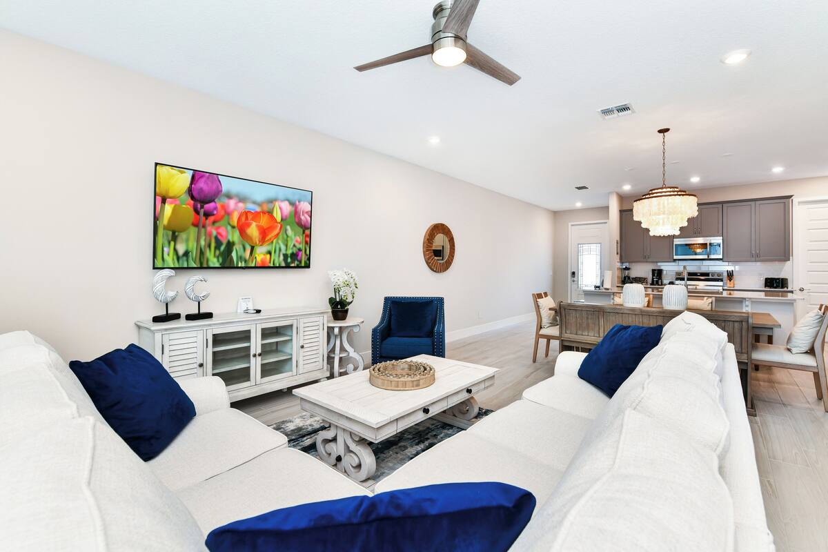 A modern living room with a white sofa, blue cushions, a coffee table, and a painting of tulips.