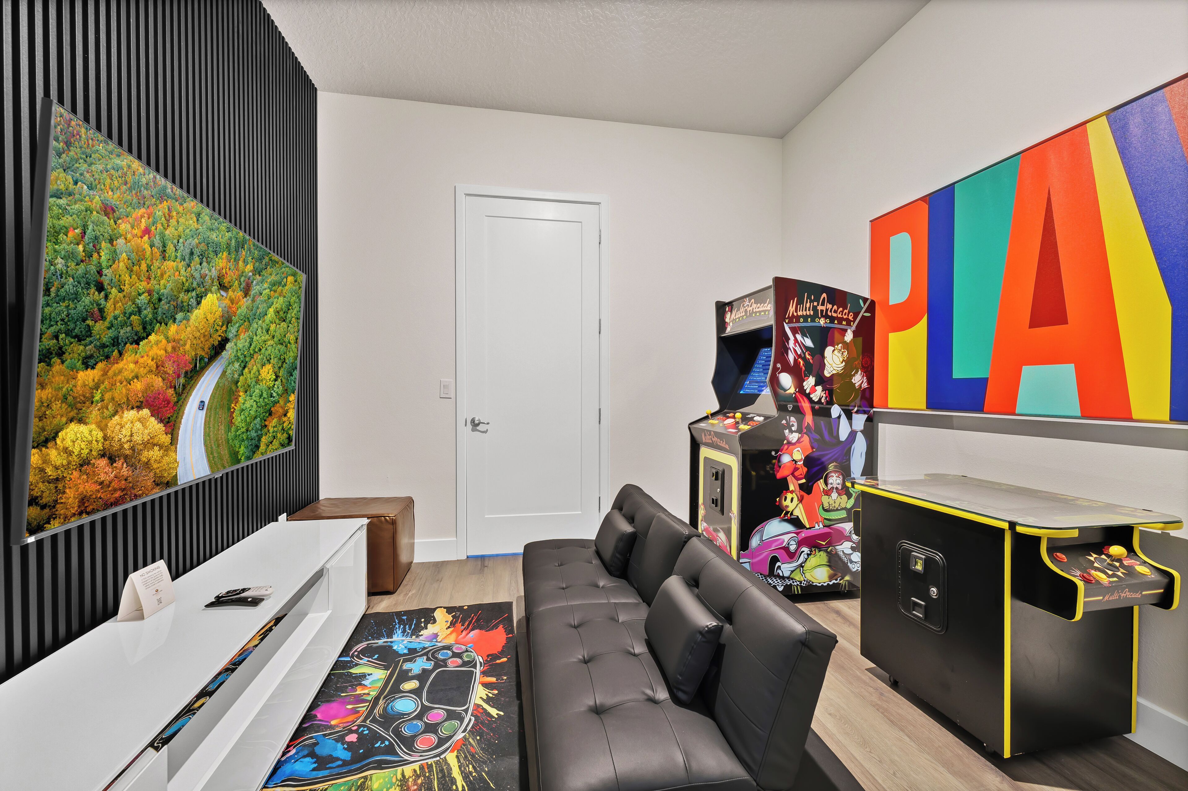 A modern room with a sofa, a desk, a colorful painting, and a game machine.