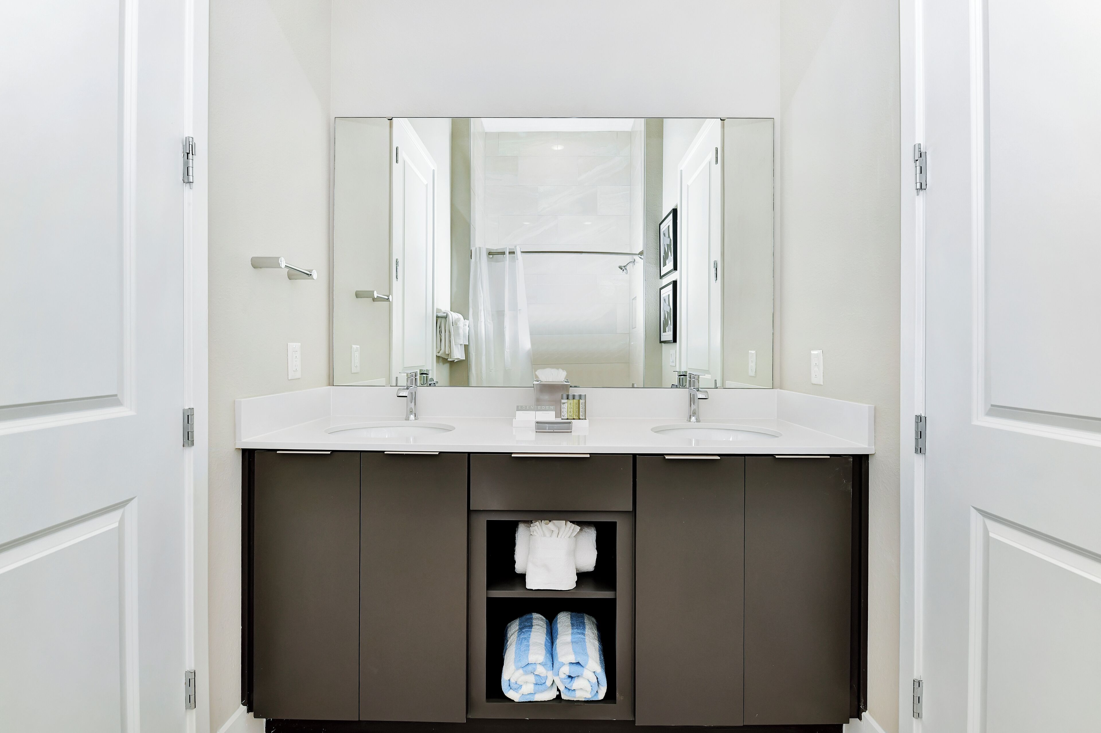 A modern bathroom with two sinks, a large mirror, and a dark cabinet with towels.