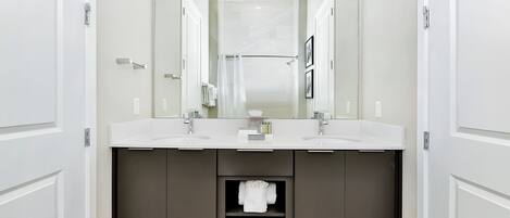A modern bathroom with two sinks, a large mirror, and a dark cabinet with towels.