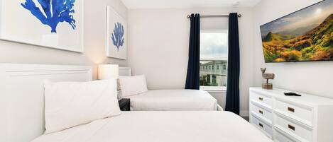 A bedroom with two beds, a ceiling fan, a TV, and artwork on the walls.
