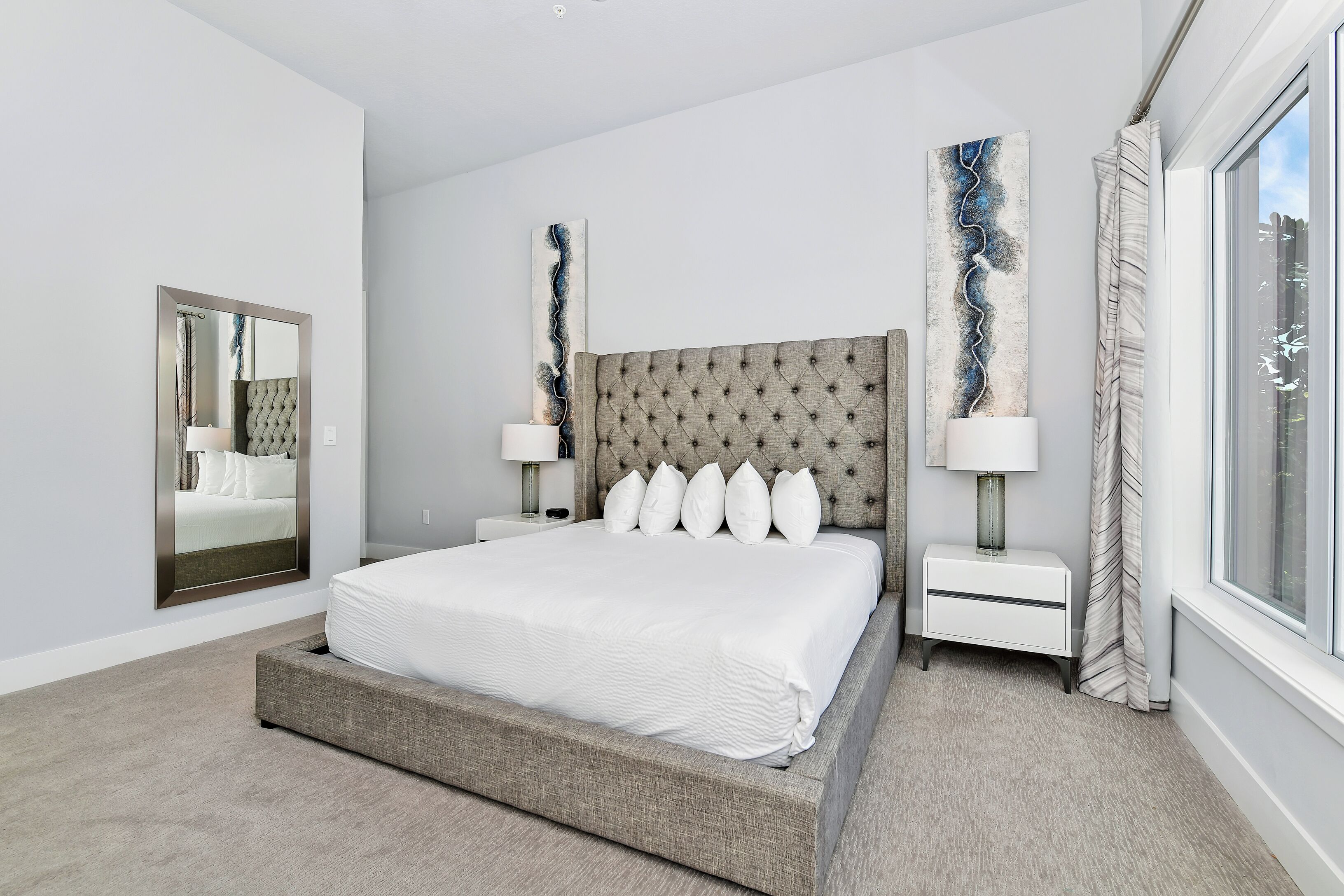 Ein modernes Schlafzimmer mit einem großen Bett, zwei Nachttischen, einem Spiegel und abstrakter Wandkunst.