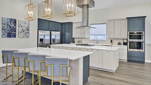 A modern kitchen with a central island, bar stools, stainless steel appliances, and pendant lighting. - Spectrum Resort Villas Orlando and Waterparks (Kissimmee)
