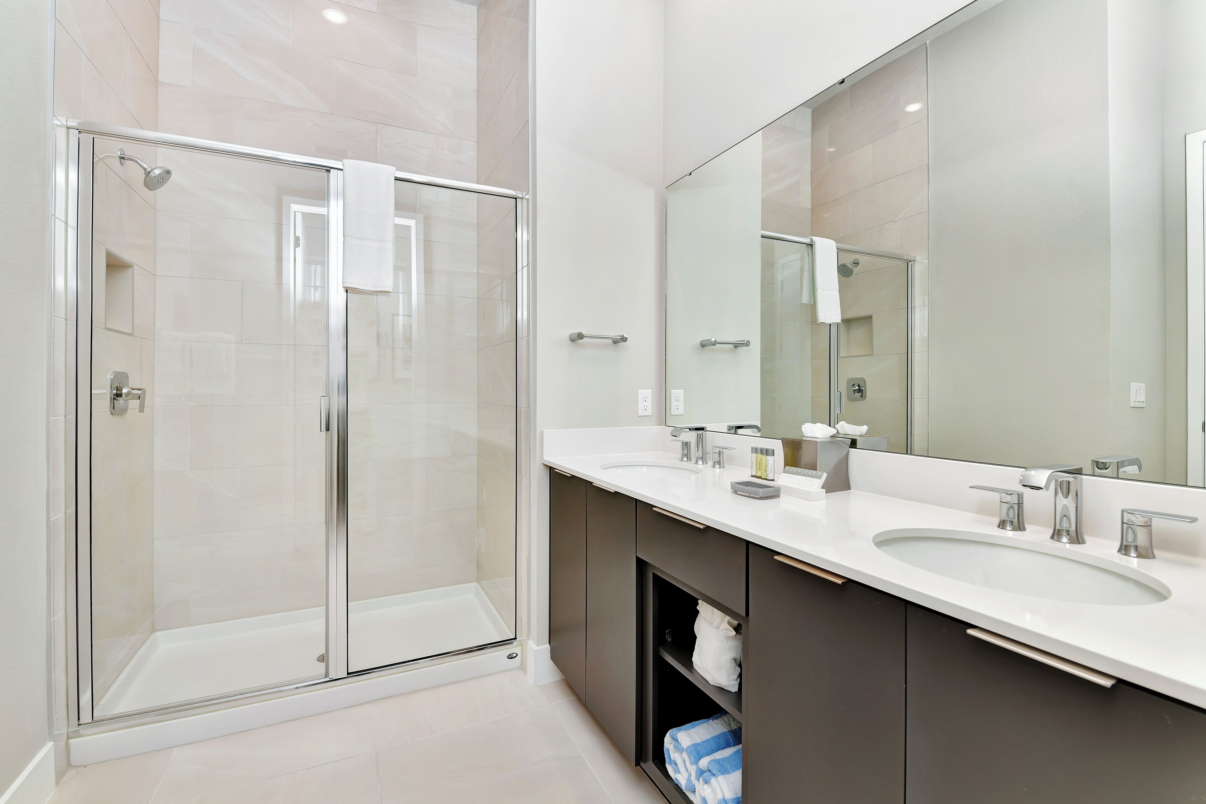 Een moderne badkamer met een douche met glazen wand, een grote spiegel en een wastafel met twee kommen.