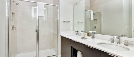 Een moderne badkamer met een douche met glazen wand, een grote spiegel en een wastafel met twee kommen.
