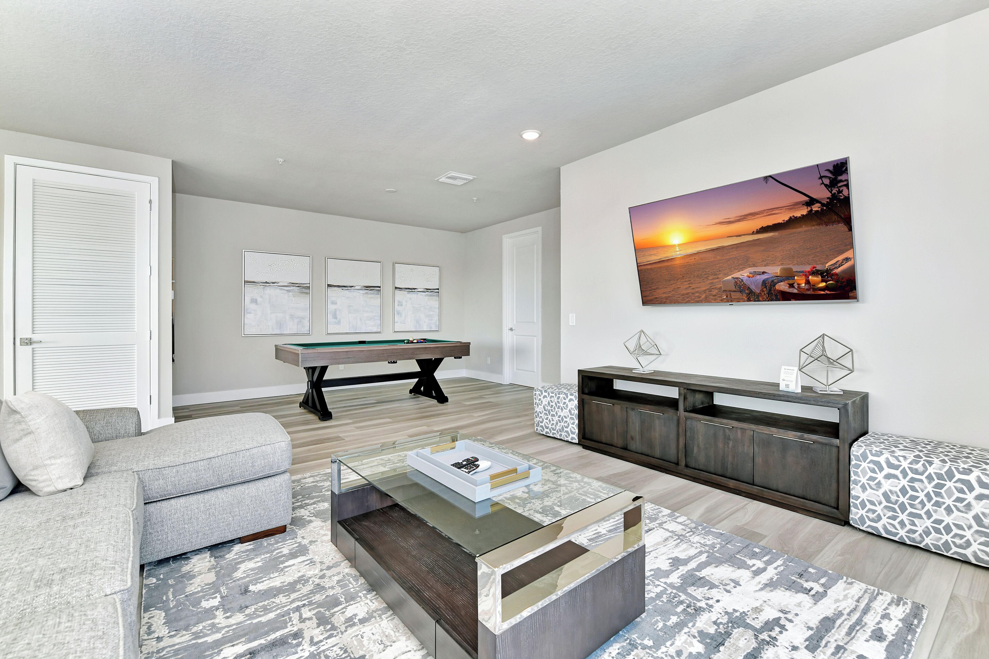 A modern living room with a pool table, a sofa, a coffee table, and a large wall-mounted TV.