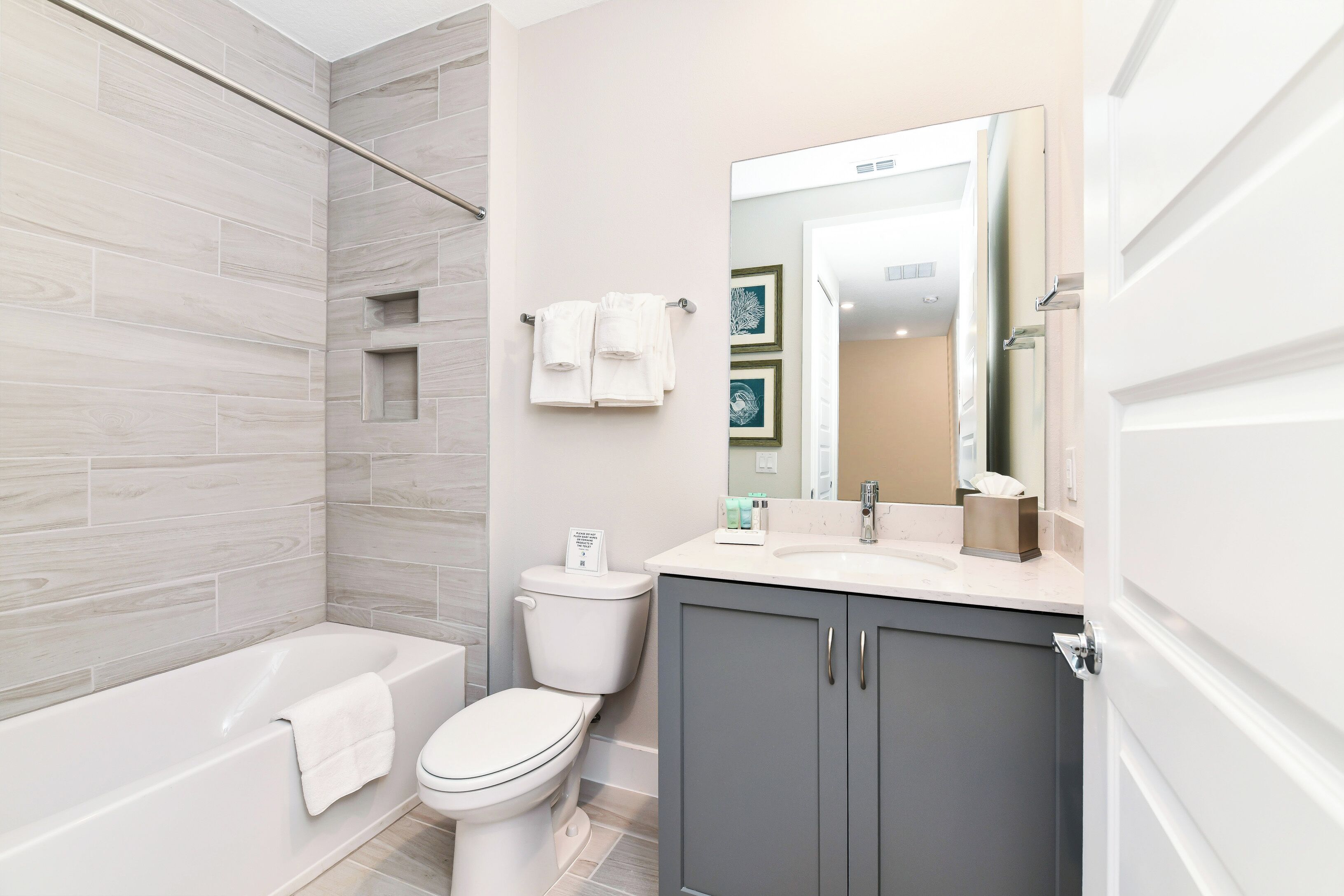 A modern bathroom with a bathtub, toilet, vanity, and a large mirror.
