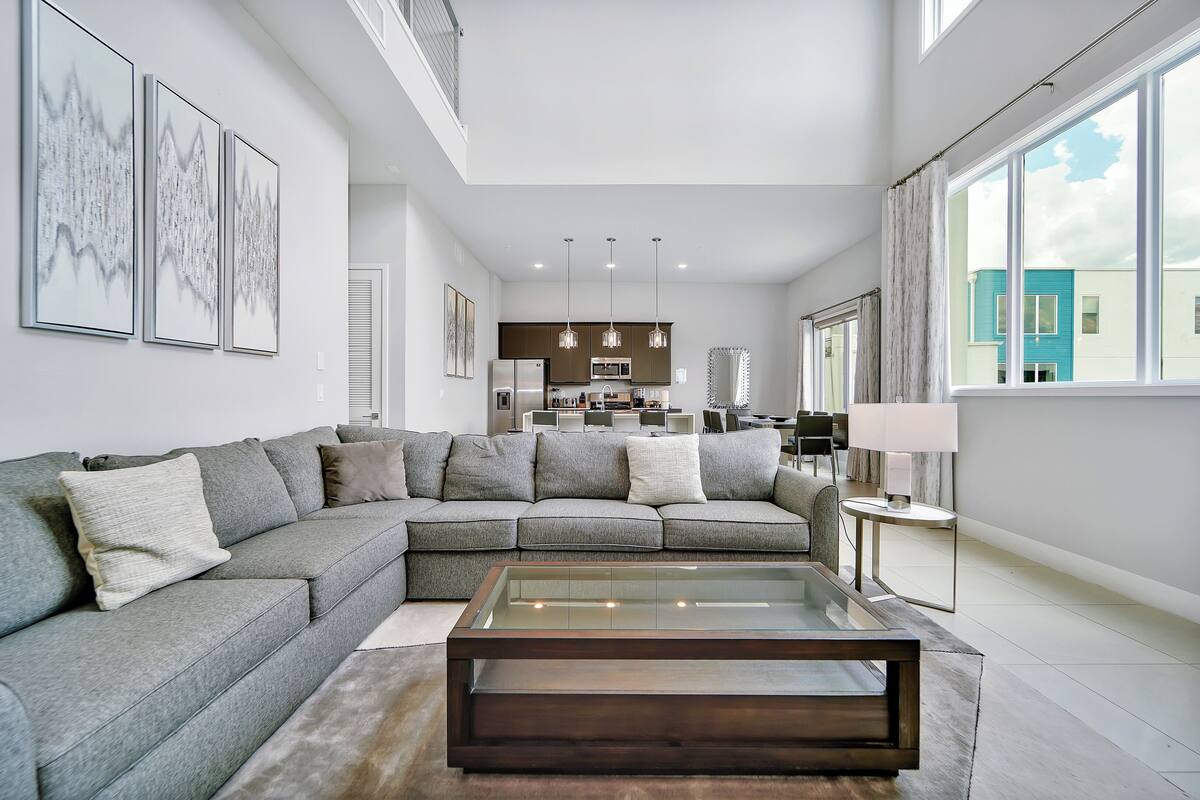 A modern living room with a sectional sofa, a glass coffee table, and a kitchen in the background.