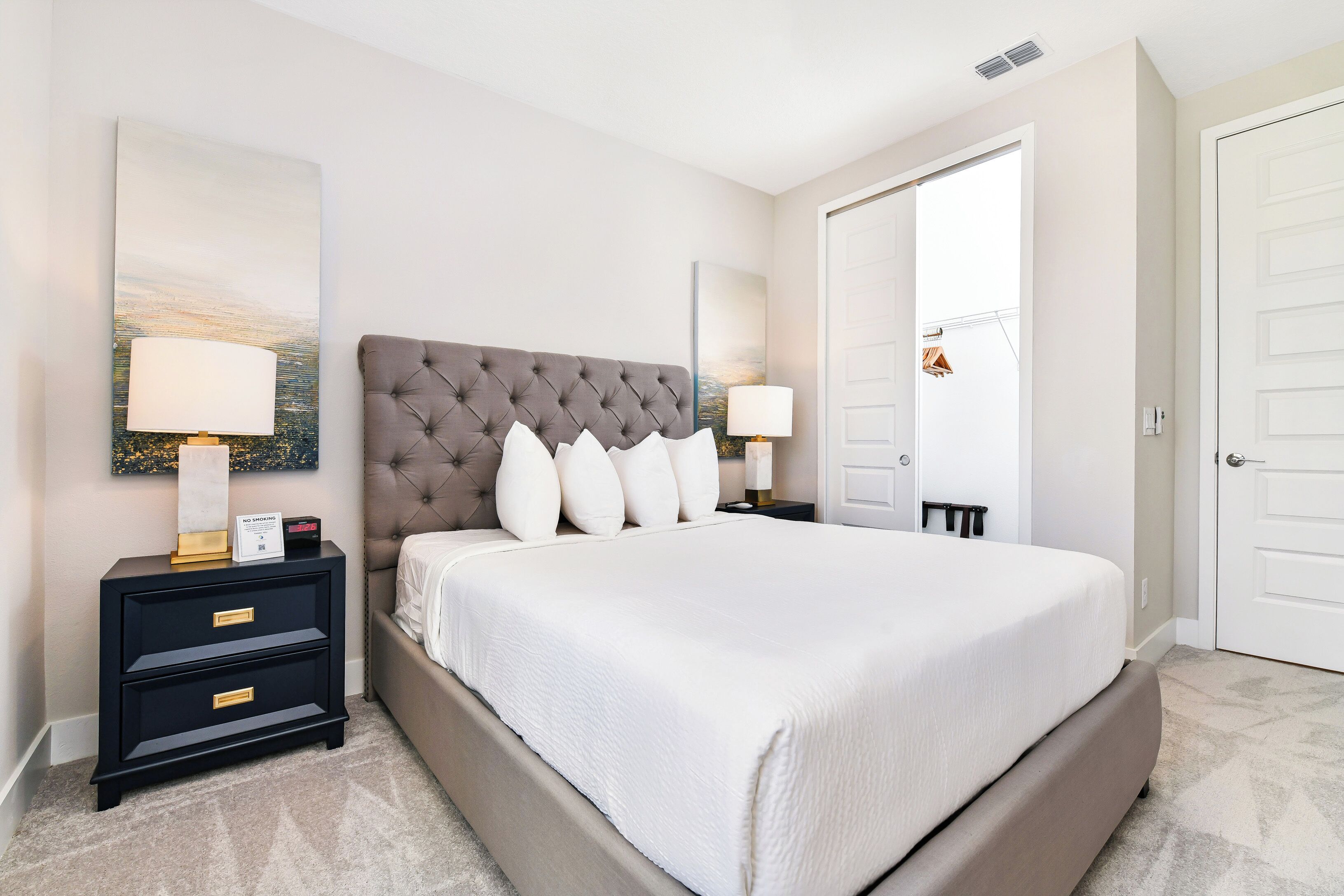 A bedroom with a tufted headboard, a large bed with white bedding, two bedside tables with lamps, and a door in the background.