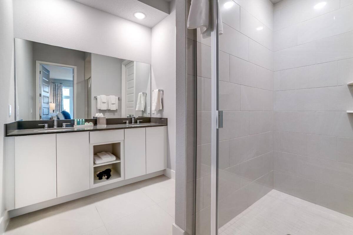 A modern bathroom with a glass shower enclosure, a large mirror, and a white vanity with a black countertop.