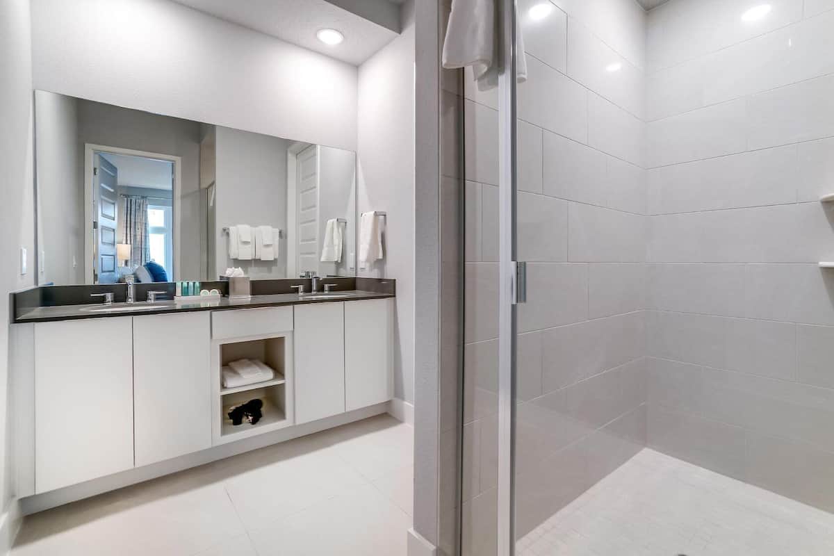A modern bathroom with a glass shower enclosure, a large mirror, and a white vanity with a black countertop.