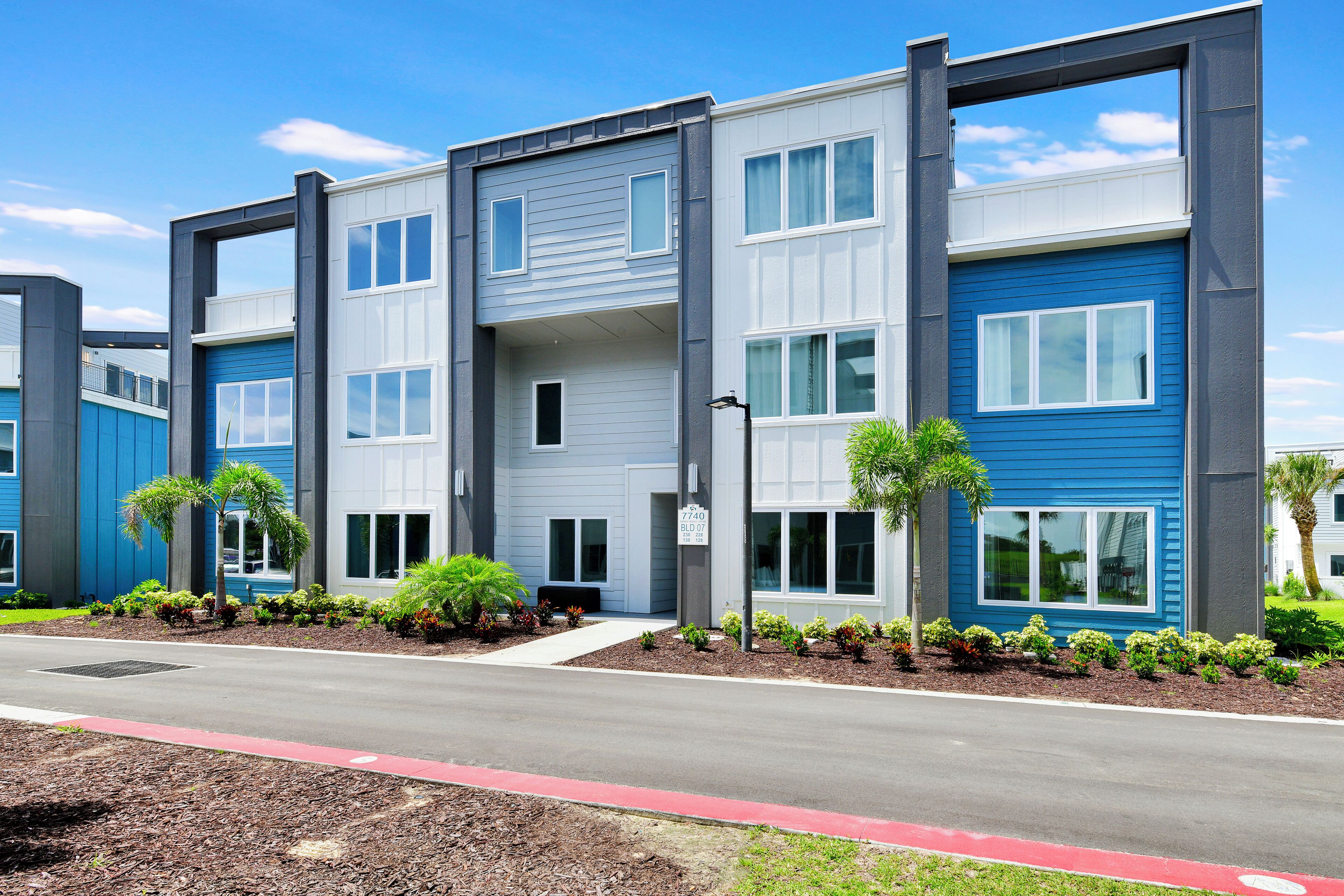 A modern multi-story residential building with a flat roof, large windows, and a well-maintained landscaped front yard.