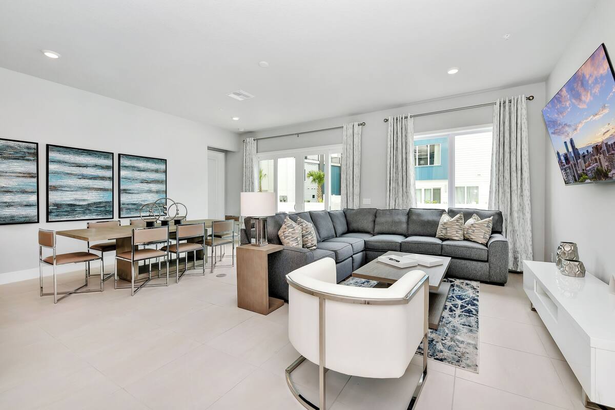 A modern living room with a grey sectional sofa, a white coffee table, and a dining area with a wooden table and chairs.