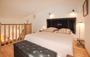 A bedroom with a large bed, a wooden bench, a nightstand, and a wall-mounted lamp. - Homerez - Villa in Montséret (Montséret)