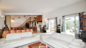 Amplia sala de estar con dos sofás blancos, una mesa de centro de madera y una escalera que conduce a un piso superior.