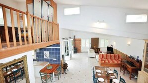 Amplia sala de estar con techo alto, escalera de madera, mesa de comedor, sofá y televisor.