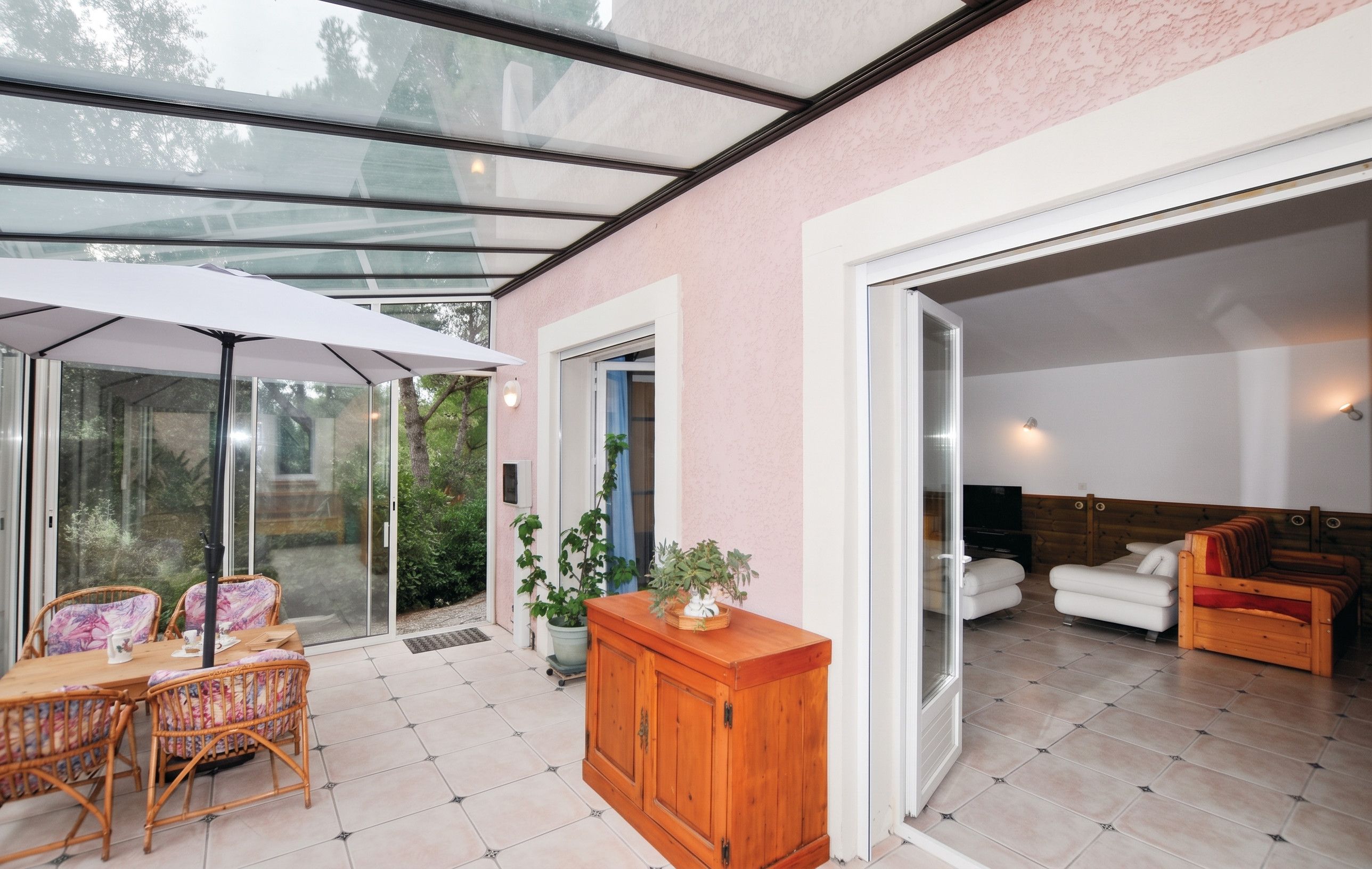 A modern interior with a glass ceiling, a dining area with wicker furniture, and a living room with a sofa and TV.