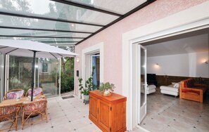 Un intérieur moderne avec un plafond en verre, un coin repas doté de meubles en osier et un salon avec un canapé et un téléviseur.