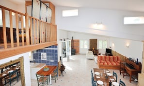 A spacious living area with a high ceiling, a dining area with a wooden table and chairs, and a cozy seating area with a sofa. - Homerez - Villa in Montséret (Montséret)