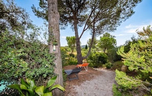 Un jardin avec un chemin de gravier, deux fauteuils de jardin et une variété d’arbres et d’arbustes.