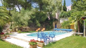 Zona de piscina con sillas azules y una pared de piedra.