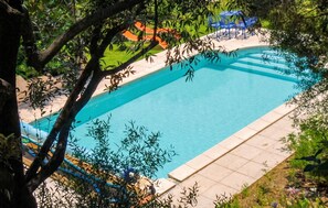 Une piscine dotée d’une terrasse carrelée, entourée de verdure et agrémentée de mobilier d’extérieur.